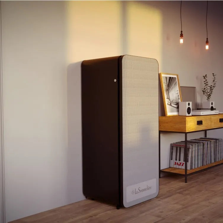 Geschlossener Weinkühler La Sommelière APOGEE150N in einem modernen Raum mit Holzboden, daneben ein Holzschreibtisch mit Lautsprechern und Vinylschallplatten, Sonnenlicht beleuchtet die Wand.