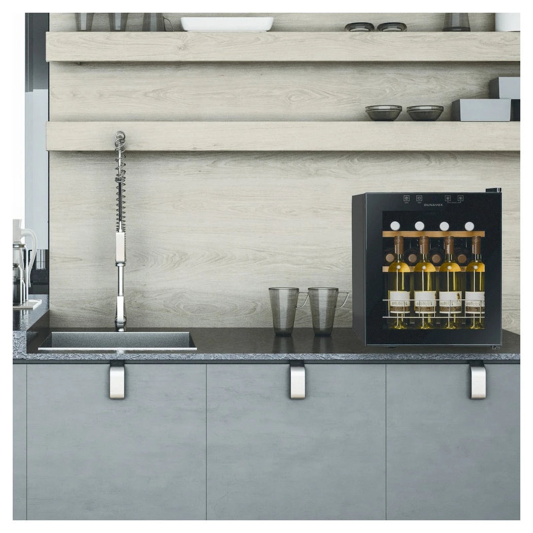 Dunavox Home-16 Weinkühlschrank freistehend auf Küchenarbeitsplatte neben Spüle, mit beladenen Weißweinflaschen sichtbar