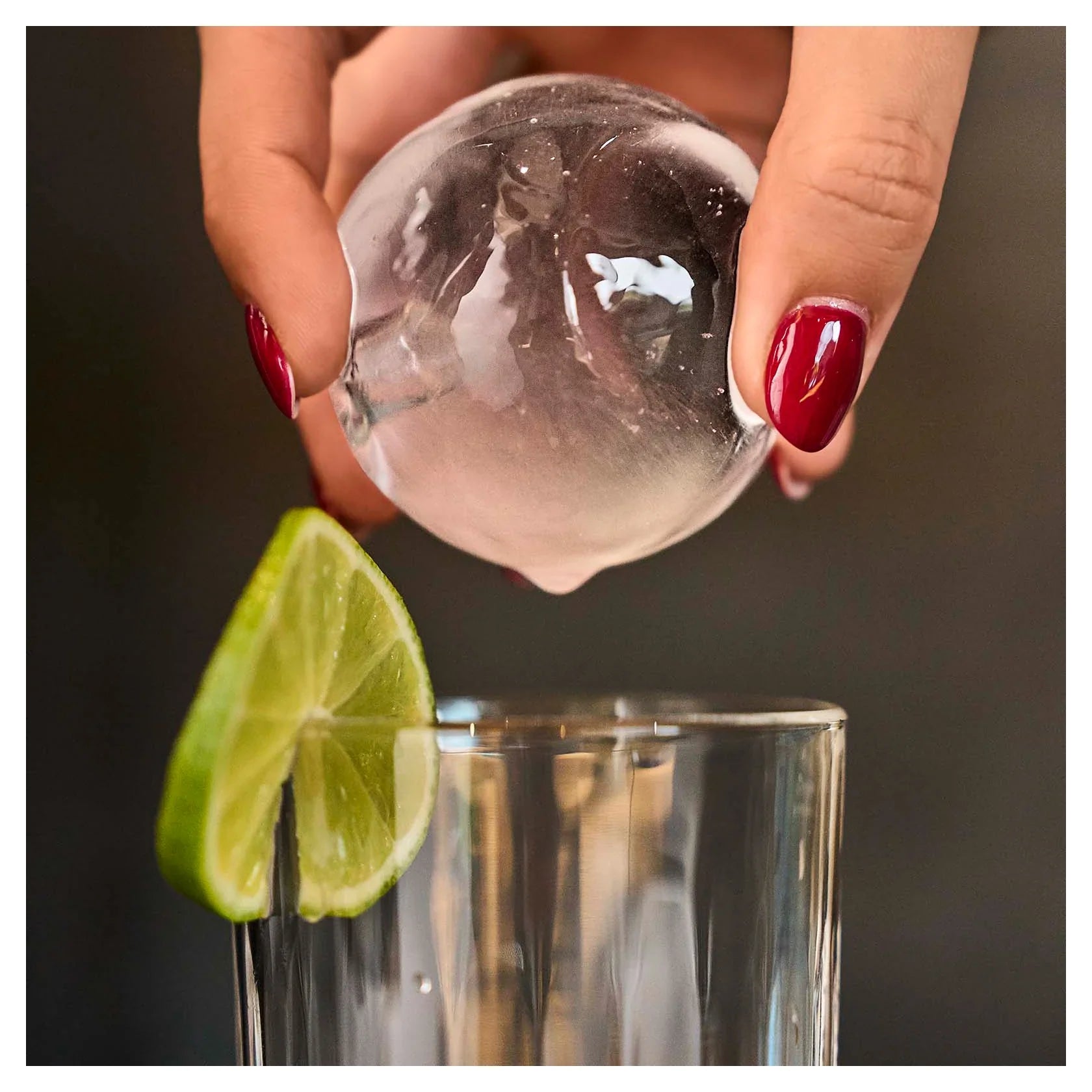 Kristallklare Eiskugel des BEEZER IceBall wird in ein Glas mit Limettenscheibe gelegt