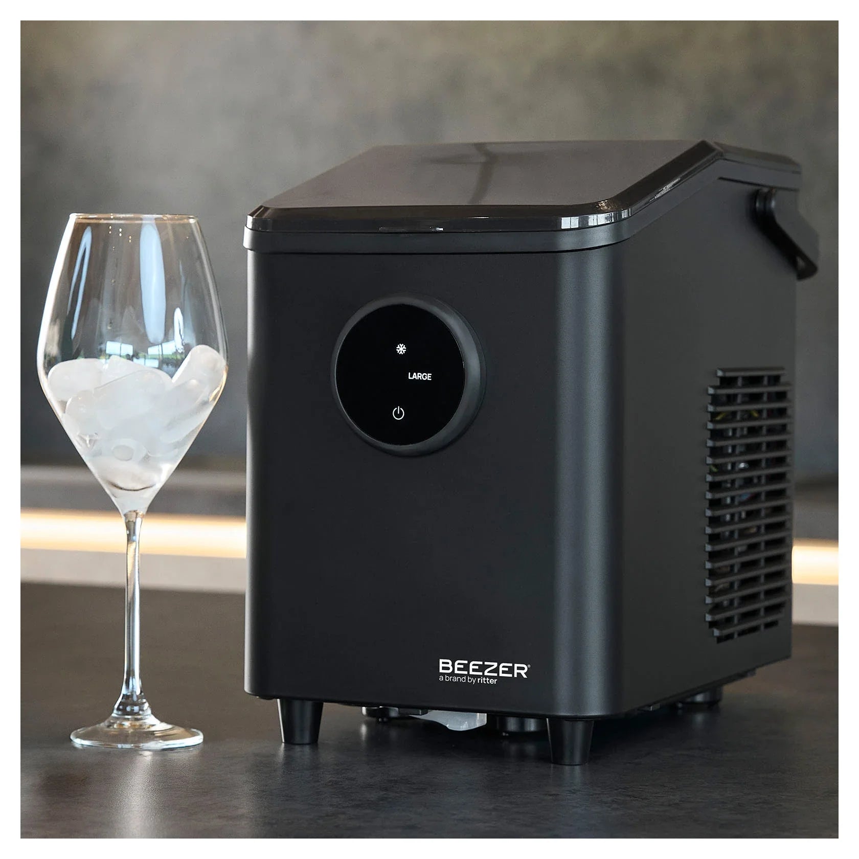 Eiswürfelbereiter BEEZER IceCube mini auf der Arbeitsplatte neben einem Glas mit Eiswürfeln